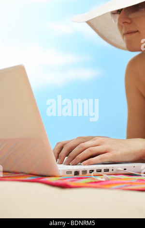 Frau mit Laptop, liegend auf Bauch am Strand, Nahaufnahme Stockfoto