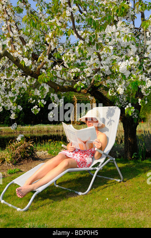 Frau liest Zeitung im Garten vor blühenden Kirschbäume Baum Stockfoto