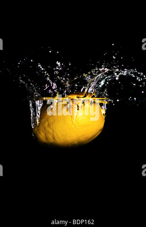 Eine Zitrone fiel ins Wasser, einen Spritzer und Luftblasen zu schaffen. Isoliert auf schwarz. Stockfoto