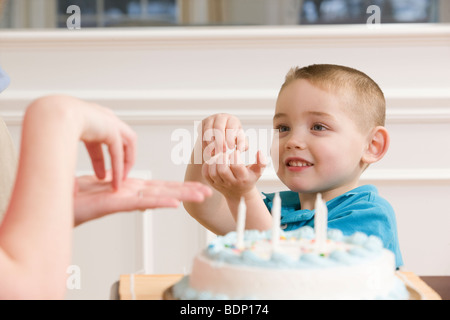Junge Unterzeichnung das Wort "Kuchen" in amerikanischer Gebärdensprache sitzt vor einem Geburtstagskuchen Stockfoto