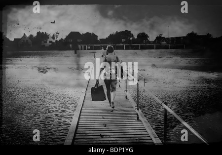 Eine Frau mittleren Alters tragen einen Badeanzug mit einer Tasche, einem hölzernen Steg am Meer entlang Stockfoto