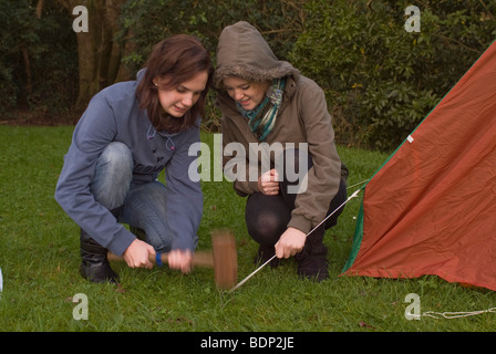 Zwei Mädchen, camping in einem Zelthering befestigt, die Abspannseile ein Notzelt hämmern. Stockfoto