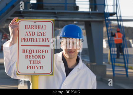 Labor-Mitarbeiter neben einer Warnung Schild mit der Aufschrift "Hardhat und Auge Schutz erforderlich Beyond This Point" Stockfoto