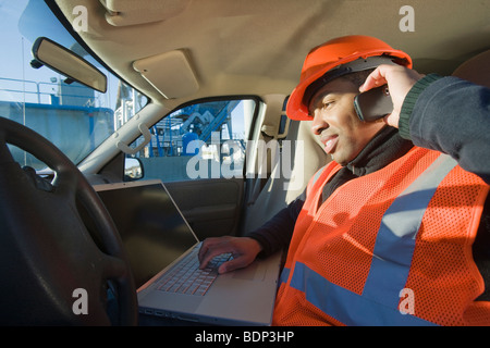 Ingenieur auf einem Laptop arbeiten und sprechen auf einem Handy im Auto Stockfoto