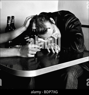 Ein junger Mann trägt eine Lederjacke, rauchte eine Zigarette mit leeren Bierflaschen auf einem Tisch Stockfoto