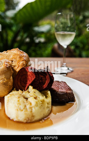 Ein Rinderbraten mit Maische Kartoffel, Yorkshire Pudding, rote Beete Chips, Soße und einem Glas Weißwein ablöschen. Stockfoto