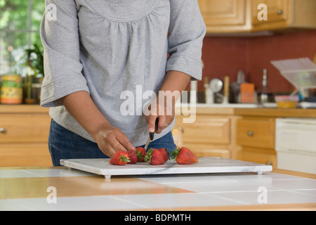 Hispanic Frau schneiden Erdbeeren in der Küche Stockfoto