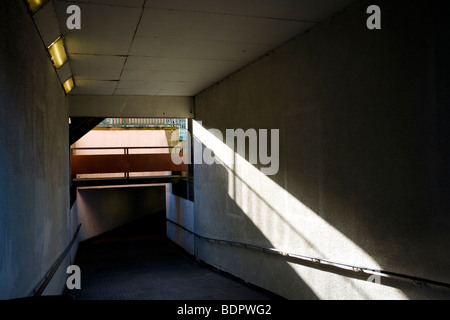 Licht und Schatten in einer städtischen Betonunterführung. Ein starker Durchgang, der geometrische Formen, starke Winkellinien und ein Gefühl der Isolation zeigt. Stockfoto