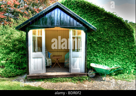 Ein kleine hölzerne Sommer Haus mit Stühlen, Tisch und eine grüne Schubkarre Stockfoto