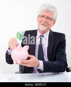 leitenden Geschäftsmann einfügen ein 100 Euro-Schein in ein Sparschwein Stockfoto