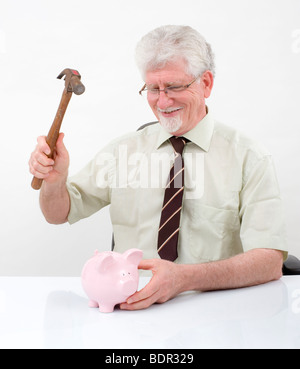 Senior Mann mit einem Hammer bricht ein Sparschwein über weiß Stockfoto