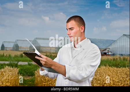 Landwirtschaft-Wissenschaftler, die Notizen auf dem Gebiet mit Gewächshäusern im Hintergrund Stockfoto