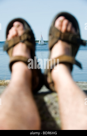 Füße mit Sandalen und ein Segelboot Schweden. Stockfoto