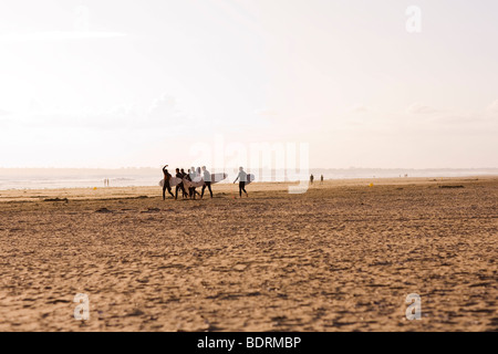 In der Ferne kann Silhouetten von Surfern zu Fuß entlang des Strandes vor den Kopf in das Meer sehen. Stockfoto