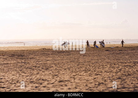 In der Ferne kann Silhouetten von Surfern zu Fuß entlang des Strandes vor den Kopf in das Meer sehen. Stockfoto