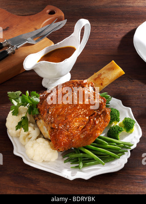 Geschmorte Kalbshaxe mit grünen Bohnen, Brokkoli, Blumenkohl und Petersilie serviert auf einem Teller mit einer Sauciere auf einem Holztisch Stockfoto