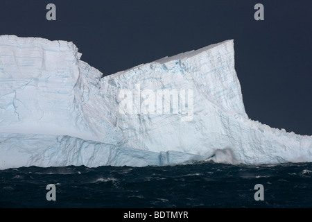Riesige Blaue Eisberge schwimmen um South Georgia Island in der antarktischen Region im November raue See, große Wellen erscheinen an der Basis des Eisbergs kleine Stockfoto
