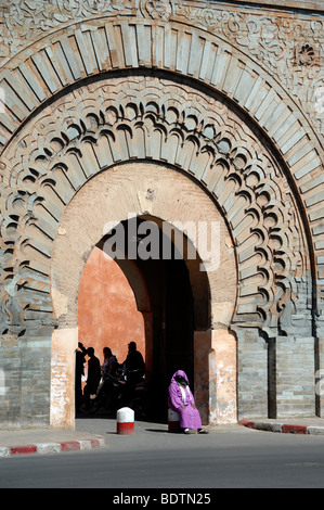 Eine verschleierte marokkanischen Frau sitzt vor der geschnitzten Stein Bab Agnaou Tor oder Eingang in der Stadtmauer von Marrakesch, Marokko Stockfoto