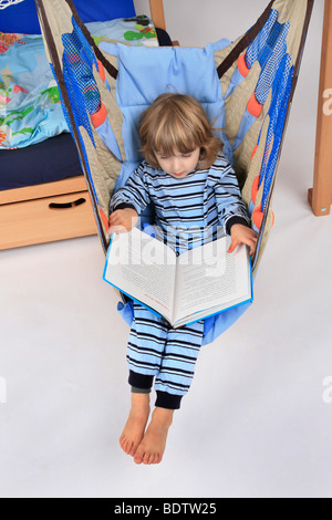 kleiner Junge im Pyjama liest ein Kinderbuch in einem Schwung ein Billi-Bolli Hochbett Stockfoto