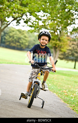 Vertikale Nahaufnahme Portrait eines jungen Mannes, der sein neues Fahrrad mit Stabilisatoren im park Stockfoto