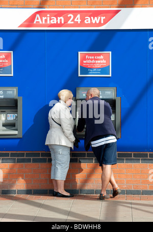 Mann und Frau mit einem Geldautomaten an einem Seitenarm des Tesco Stockfoto