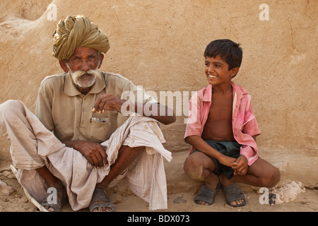 Wüste Thar, Indien eine alte Rajput Dorfbewohner beedi raucht eine Zigarette, während ein Junge lächelt und sieht auf. Stockfoto