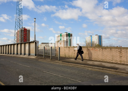 Ein Mann in einem Anzug mit einer Tasche geht um Vergangenheit Hochhaus Wohnblock in Hull Innenstadt arbeiten. Stockfoto