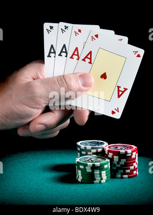 Eines Mannes Hand, die vier Asse über drei Pfähle verschiedenfarbige Chips auf einer grünen Filz. Stockfoto