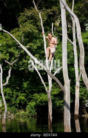 Ein Mann thront auf einem abgestorbenen Baum über dem Fluss Sioule (Puy de Dôme - Auvergne - Frankreich). Homme Perché Dans un Arbre Mort. Stockfoto