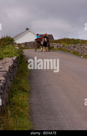 Ein Horse-drawn Wagen bewegt sich entlang einer Steinmauer gesäumten Straße auf Inis Mor (Inismore) Insel, Aran-Inseln, Co. Galway, Irland Stockfoto