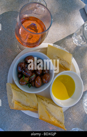 Vorspeise von biologisch angebauten Oliven, Olivenöl und knuspriges Brot mit einem Glas Rosé Stockfoto
