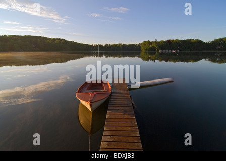 Warmen Morgenlicht erhellt eine kleine Anlegestelle und ein kleines Boot am Ufer des Sees Wesslinger sehen, Wessling, Bayern, Deutschland, E Stockfoto