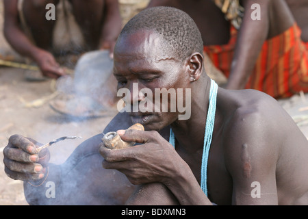 Afrika, Tansania, Lake Eyasi, Hadza Mann Rauchen AKA Hadzabe Stammes aus einer traditionellen Ton Rohr kleine Stamm der Jäger und Sammler Stockfoto