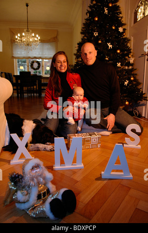 Familie mit Baby in ihrem festlich geschmückten Wohnzimmer an Weihnachten Stockfoto