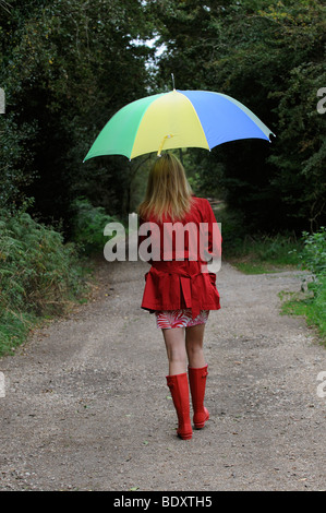Frau trägt einen roten Regenmantel und Stiefel halten einen Regenschirm Stockfoto