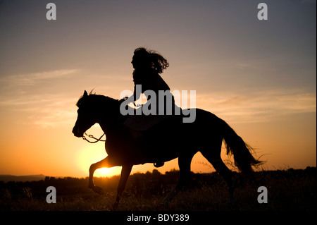 Frau reitet ihr Pferd bei Sonnenuntergang Stockfoto