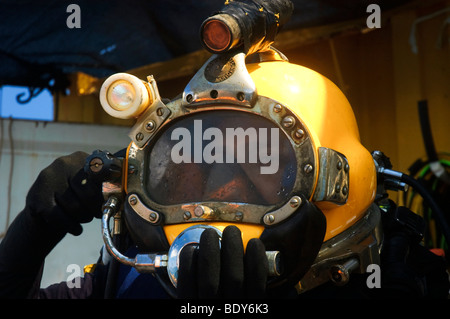 Gewerblicher Taucher macht sich bereit für einen Tauchgang, den der Taucher einen Helm, verbunden mit einer Druckluftversorgung auf seinem Rücken verwendet wird Stockfoto