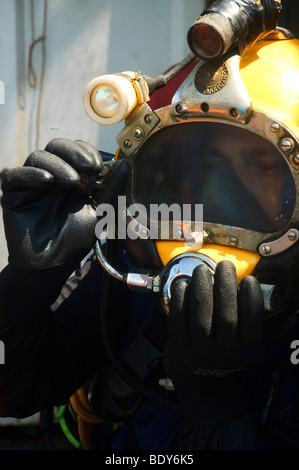 Gewerblicher Taucher macht sich bereit für einen Tauchgang, den der Taucher einen Helm, verbunden mit einer Druckluftversorgung auf seinem Rücken verwendet wird Stockfoto