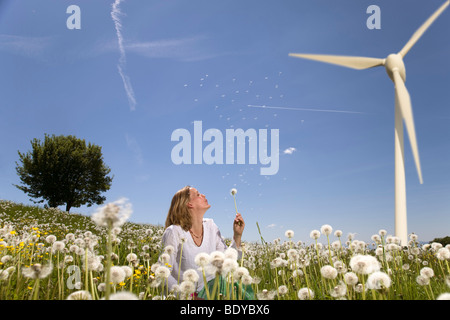 Frau bläst Löwenzahn an Windturbine Stockfoto