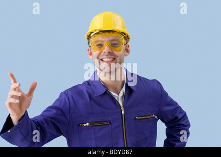 Arbeiter in einem Kessel-Anzug, einen gelben Helm und Schutzbrille gestikulierend Stockfoto
