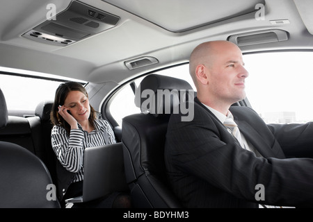 Frau im Auto mit Fahrer auf Handy Stockfoto