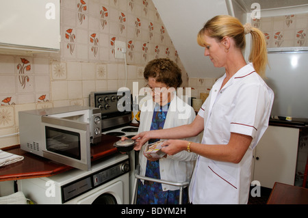 Ältere Frau in der Küche lernt kochen für eine in einem Mikrowellenherd und wird Suppervised durch eine Pflegeperson Stockfoto