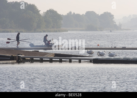 Ruderer auf einem Steg und Reisebus in einem Motorboot im Morgengrauen, Castle Semple Loch, Clyde Muirshiel Regional Park, Lochwinnoch, Renfrewshire, Schottland, Großbritannien Stockfoto