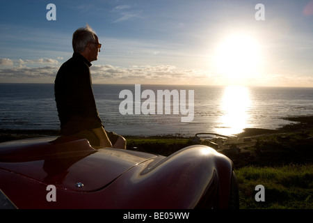 Ältere Mann Blick auf Sonnenuntergang von Motorhaube Stockfoto