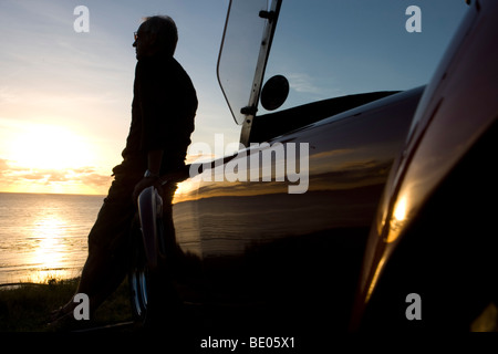 Ältere Mann Blick auf Sonnenuntergang von Motorhaube Stockfoto