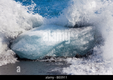 Slow-Shutter Temposchuss einer Welle brechen gegen einen Eisberg auf einem vulkanischen schwarzen Sandstrand in Island. Stockfoto