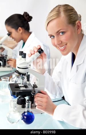Eine blonde medizinische oder wissenschaftliche Forscherin oder Arzt mit ihrem Mikroskop im Labor mit ihrem asiatischen Kollegen Stockfoto