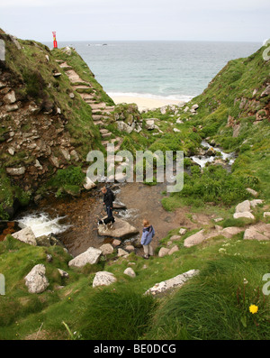 Zwei Frauen, die zu Fuß über die Treppe und Stream mit Trittsteine führt zu Portheras Cove Cornwall, England, UK Stockfoto