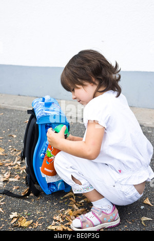 Junge Schülerin sitzt vor ihrem Ranzen, hält eine Trinkflasche Stockfoto