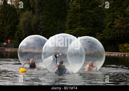 Drei junge Mädchen spielen in einem Bubblerunner über den öffentlichen See bei Rouken Glen Park, Glasgow, UK, Schottland Stockfoto